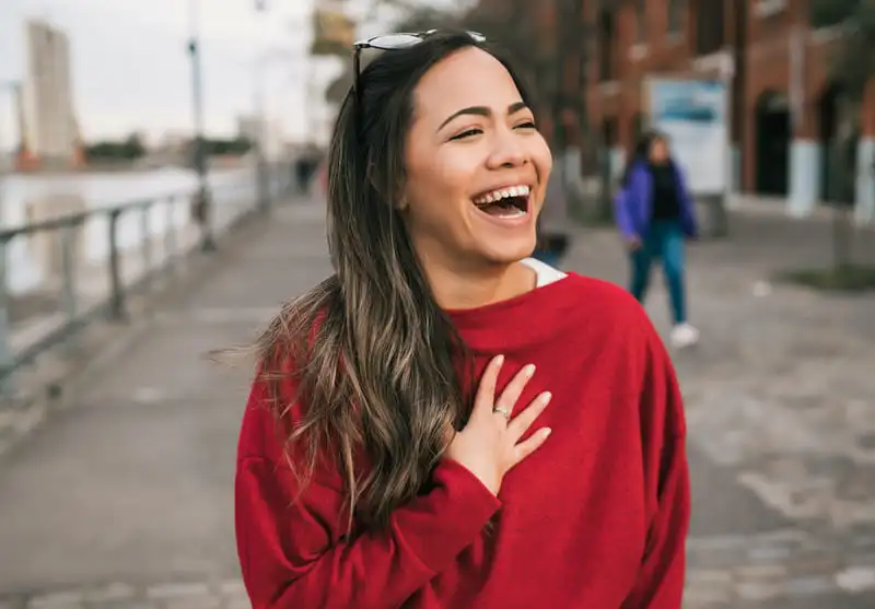 Mulher sorrindo com blusa vermelha ao ar livre, cidade ao fundo