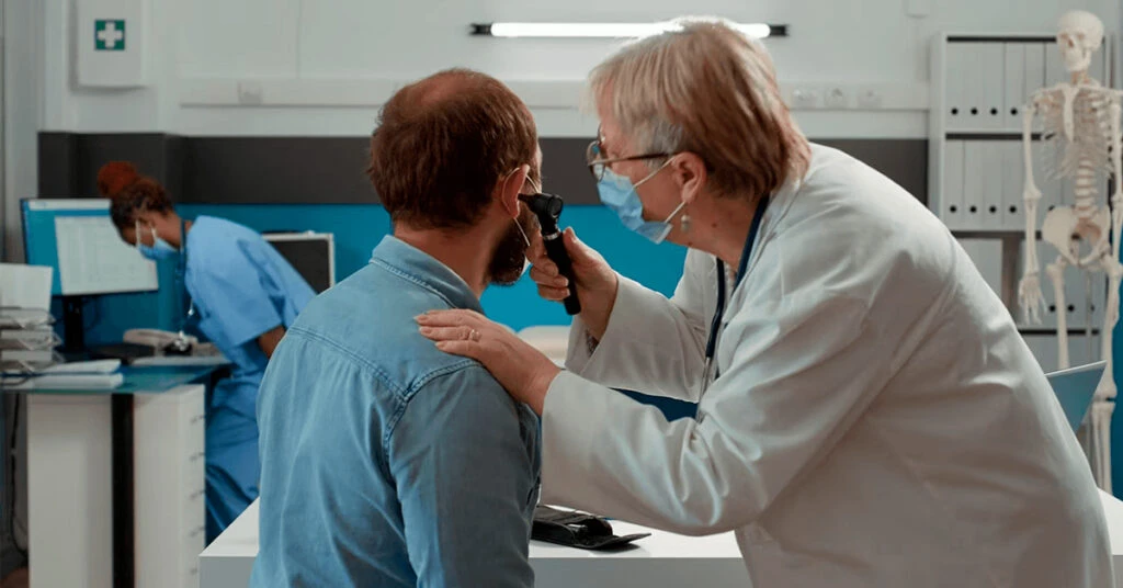 Médico realizando exame de vista em paciente em clínica oftalmológica. Profissional de saúde ajustando equipamento de ocularidade, com equipe e equipamentos no fundo.